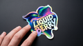 Holographic 'Liquid Berry' sticker held by a hand on a black background